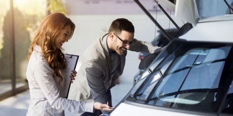 Dealership employee and smiling customer inspecting a vehicle